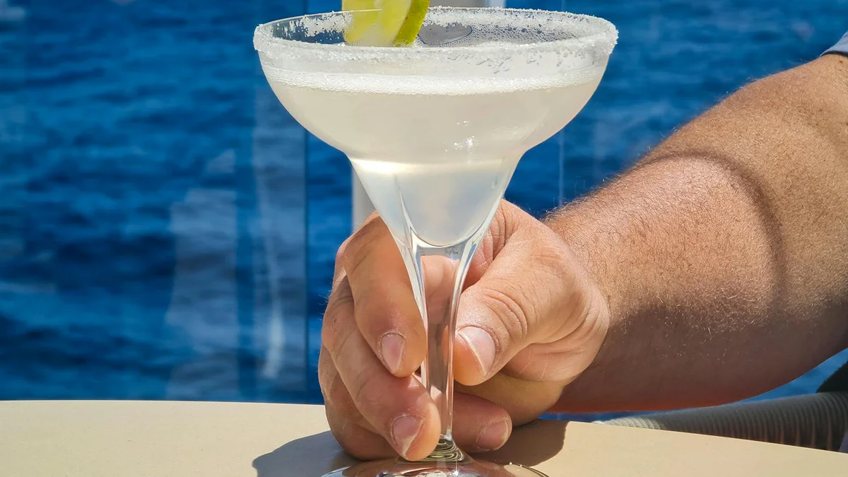 Cócteles tropicales en la cubierta de un crucero con piscina al fondo y atardecer